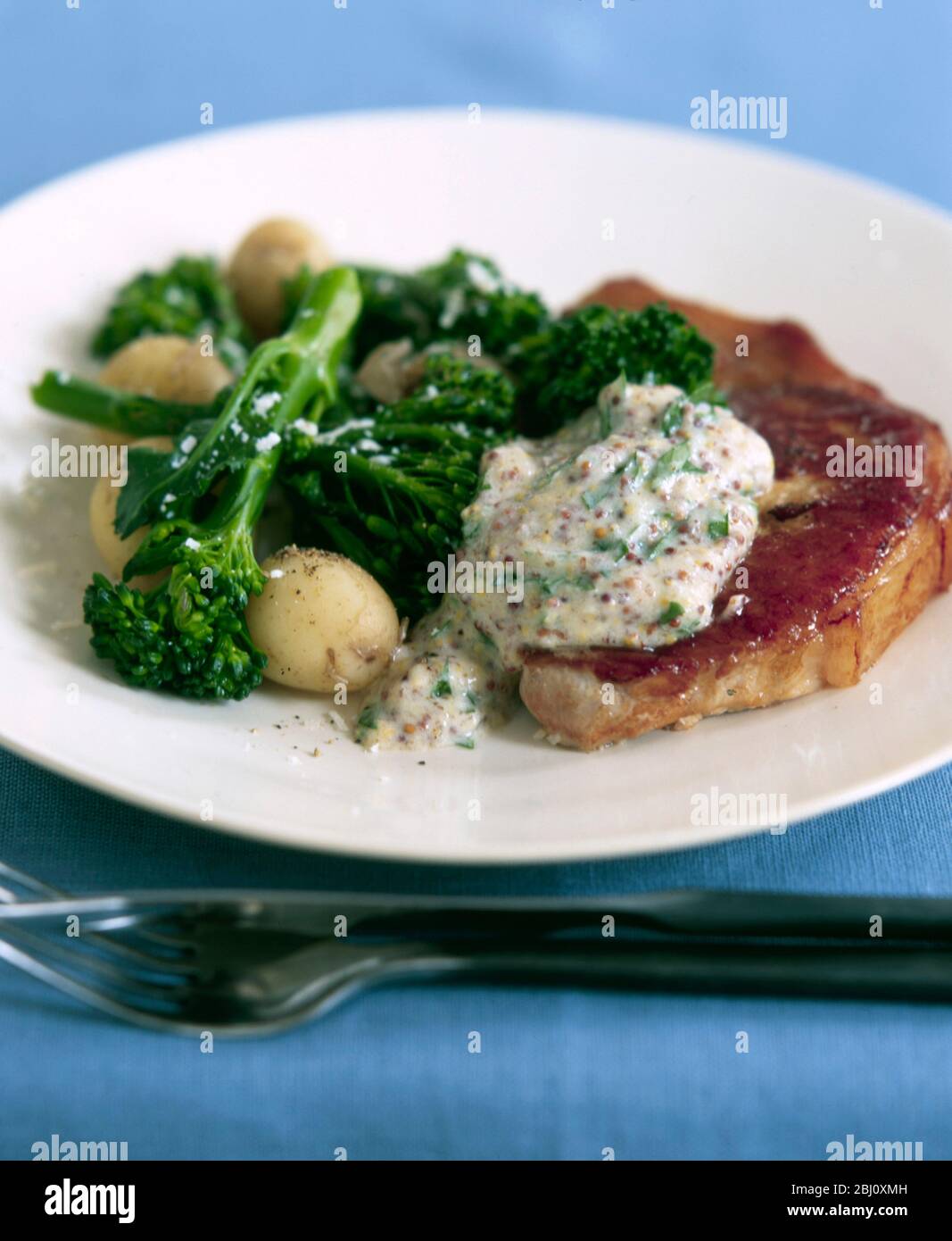 Pork chop with wholegrain mustard sauce, brocolli and new potatoes - Stock Photo