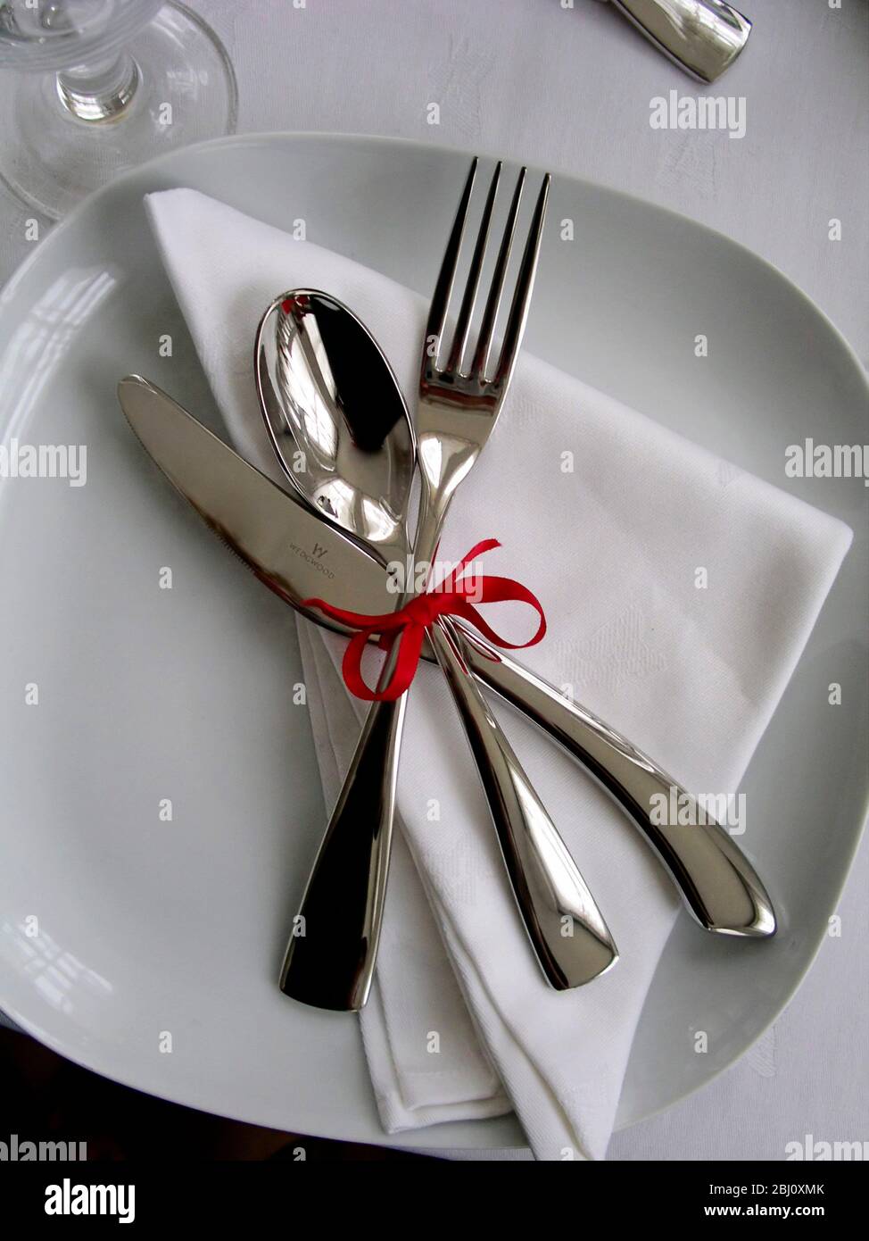 Cutlery tied with red ribbon on napkin as place setting idea - Stock Photo