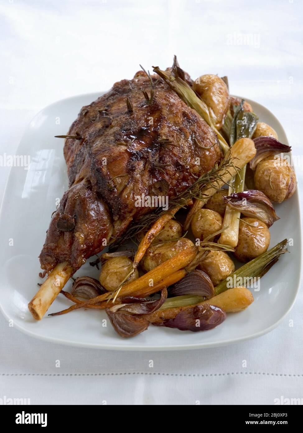 Leg of lamb on serving platter with roast new potatoes in their skins. - Stock Photo