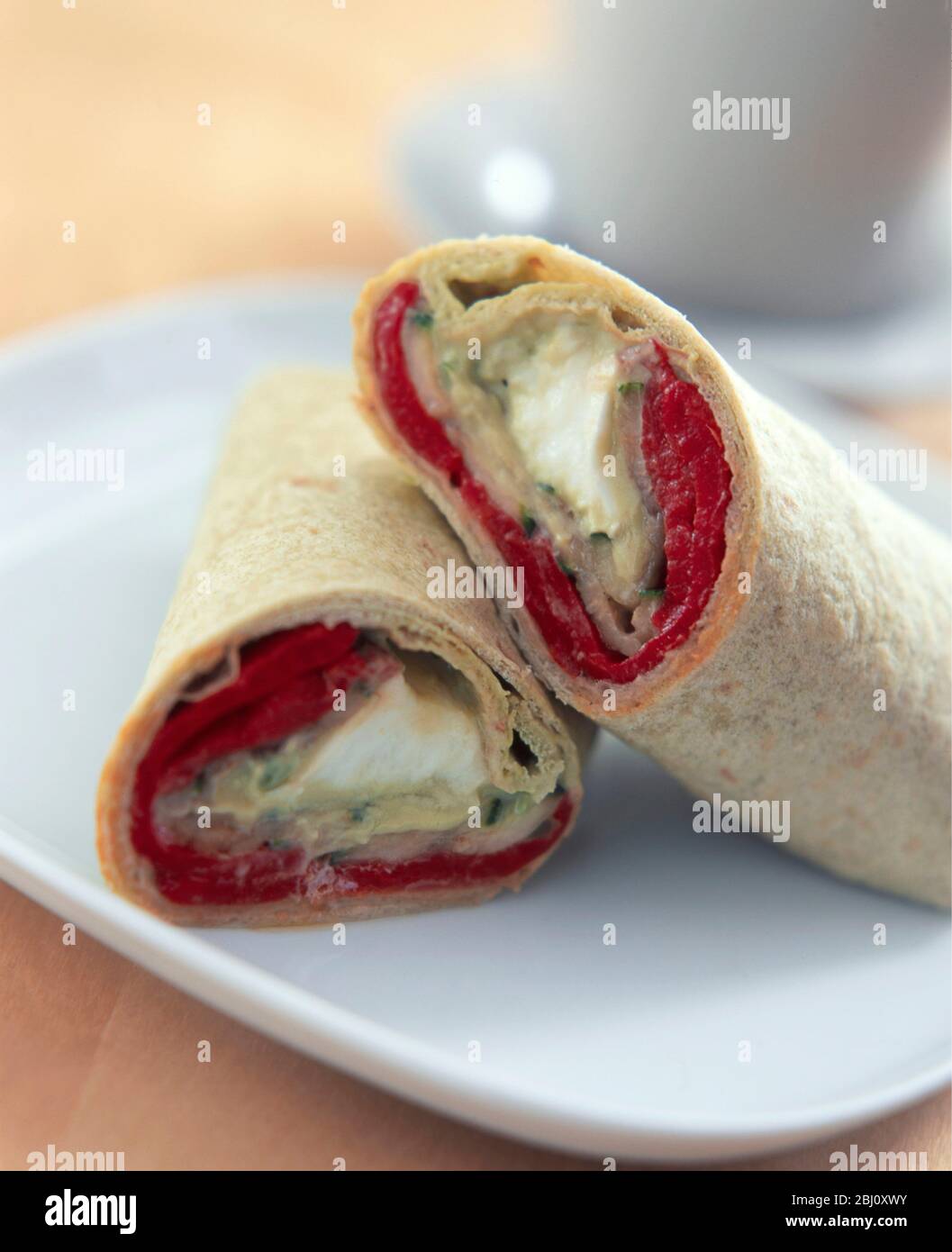 Wrap sandwich cut in two arranged on white plate with cup and saucer behind - Stock Photo