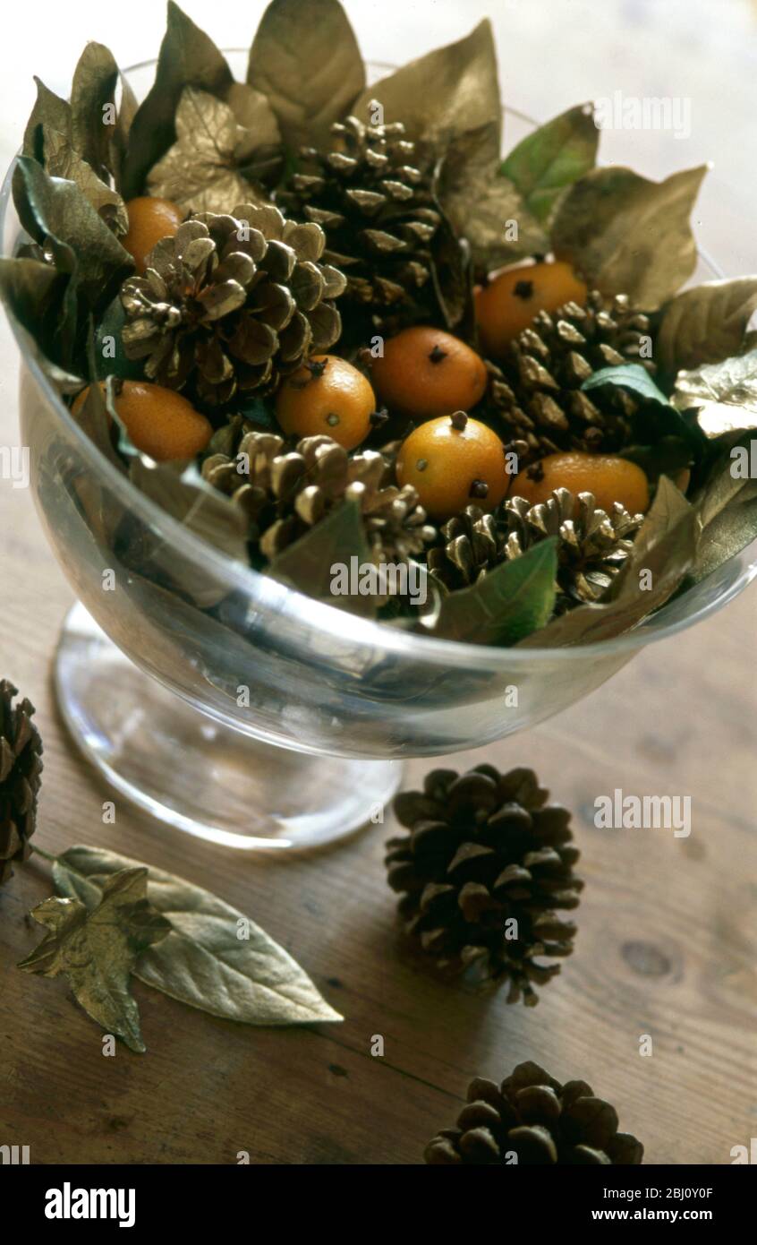Christmas decoration bowl with gilded leaves, fir cones and kumquats studded with cloves. - Stock Photo