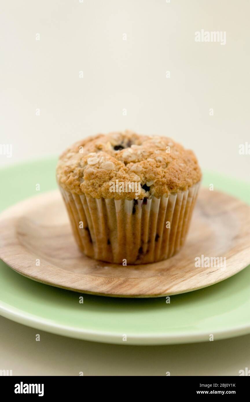 Healthy bran and raisin muffin on small wooden plate on green platter - Stock Photo