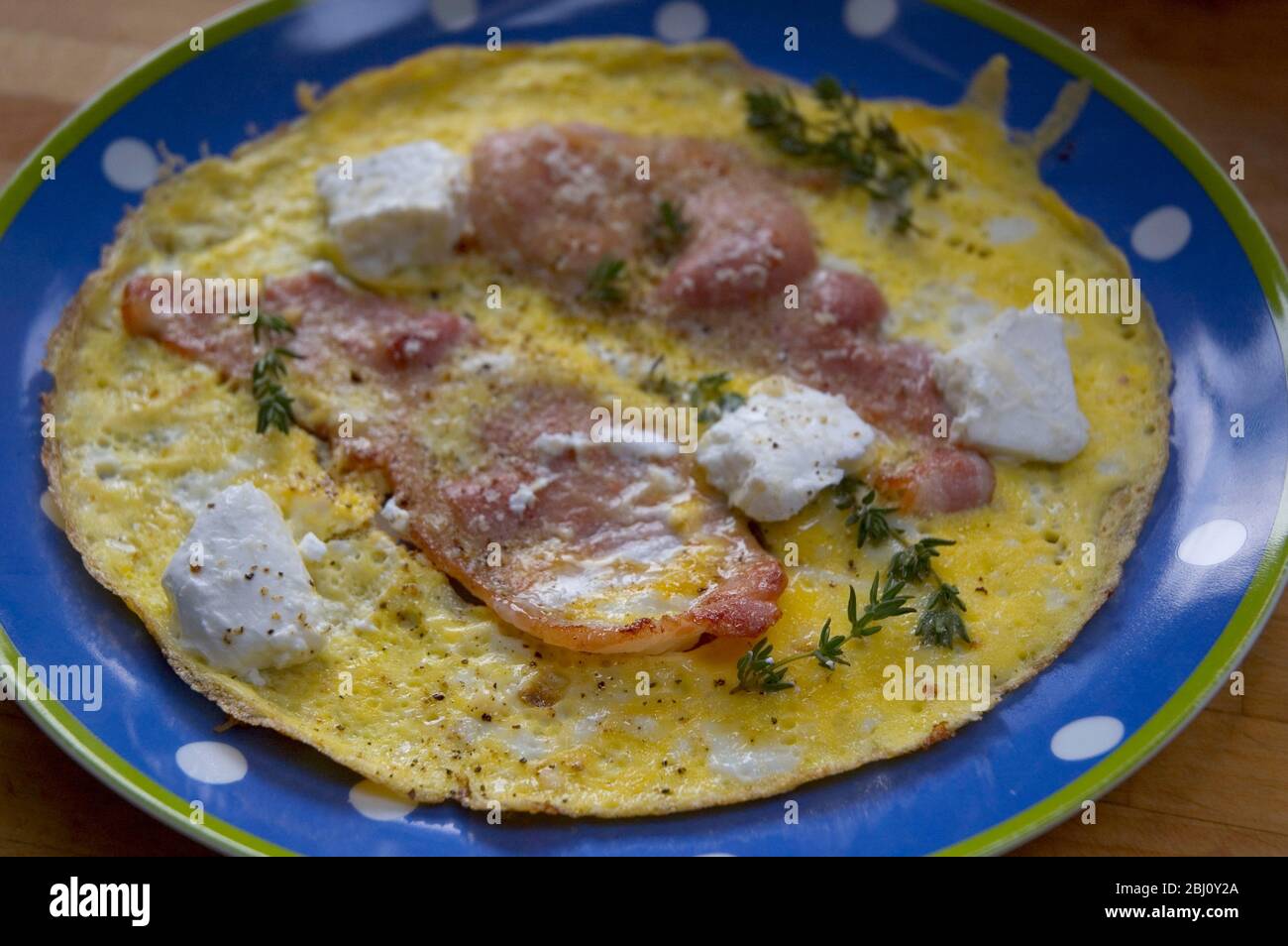 All in one breakfast omelette of eggs with bacon goat's cheese and thyme - Stock Photo