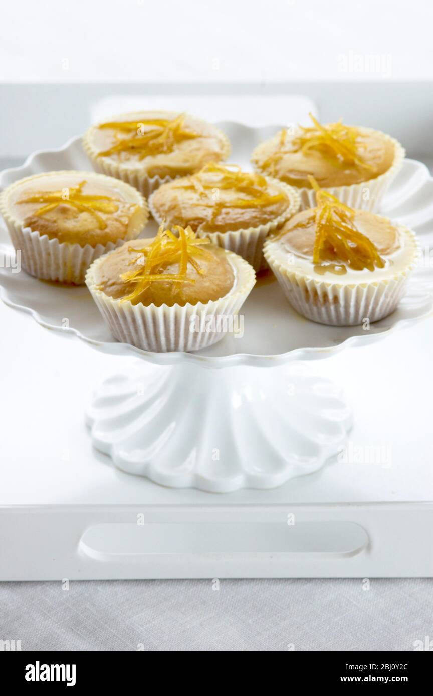Lemon muffins with lemon zest glaze on white cakestand - Stock Photo