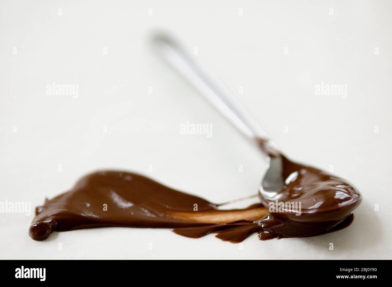 Melted chocolate on teaspoon, with smear of chocolate on greaseproof paper - Stock Photo