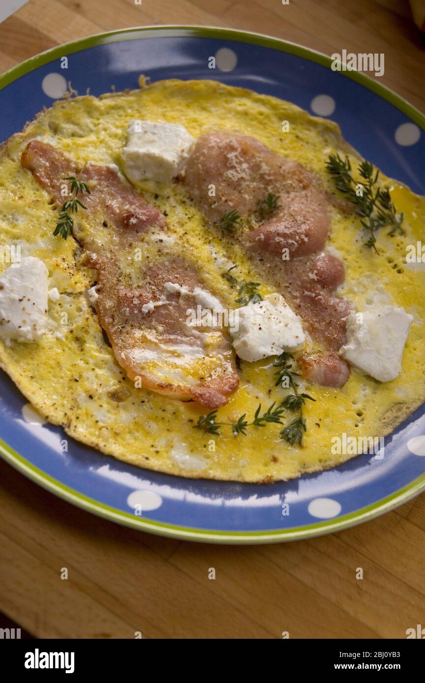 All in one breakfast omelette of eggs with bacon goat's cheese and thyme - Stock Photo