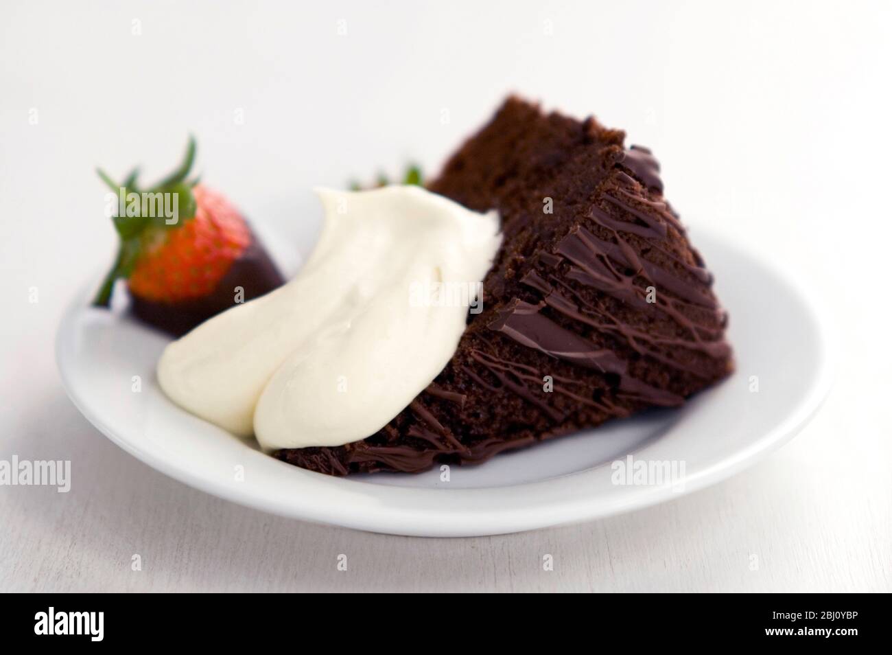 Slice of rich dark chocolate cake with dollop of cream and strawberry dipped in chocolate - Stock Photo