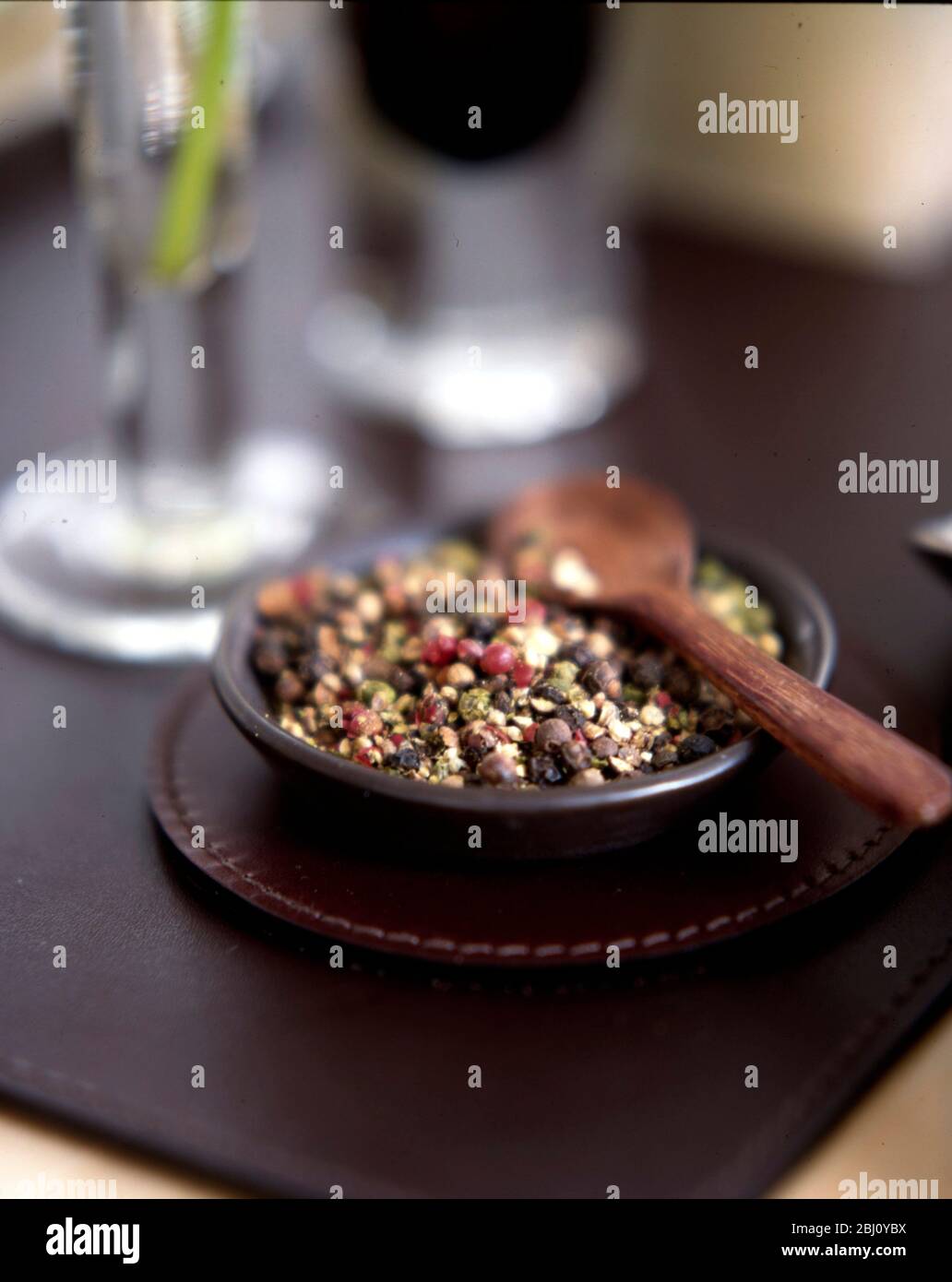 Small dish of mixed crushed peppercorns with wooden spoon - Stock Photo