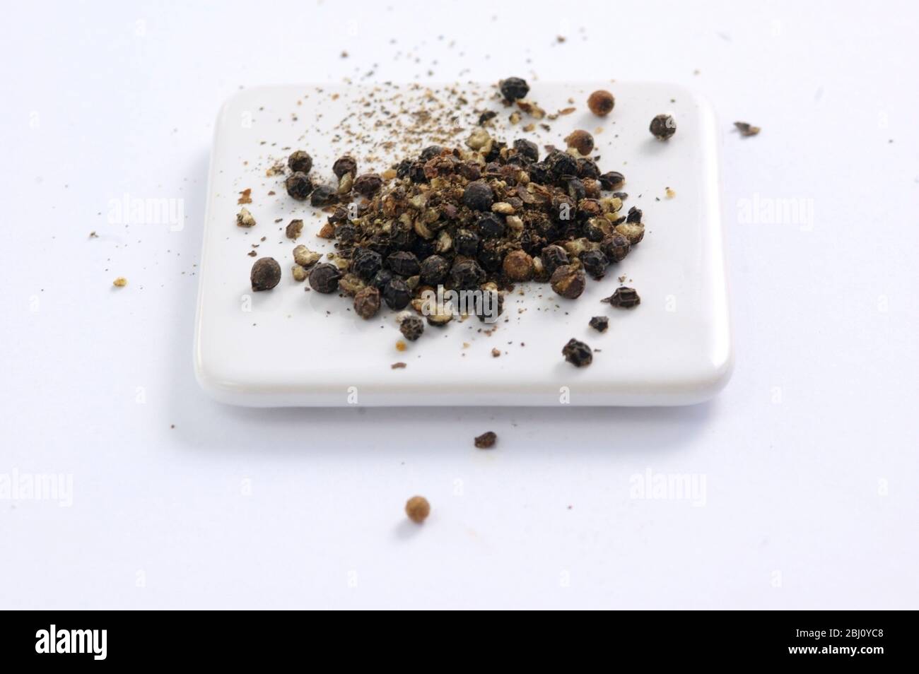 Lightly crushed black peppercorns on white surface - Stock Photo