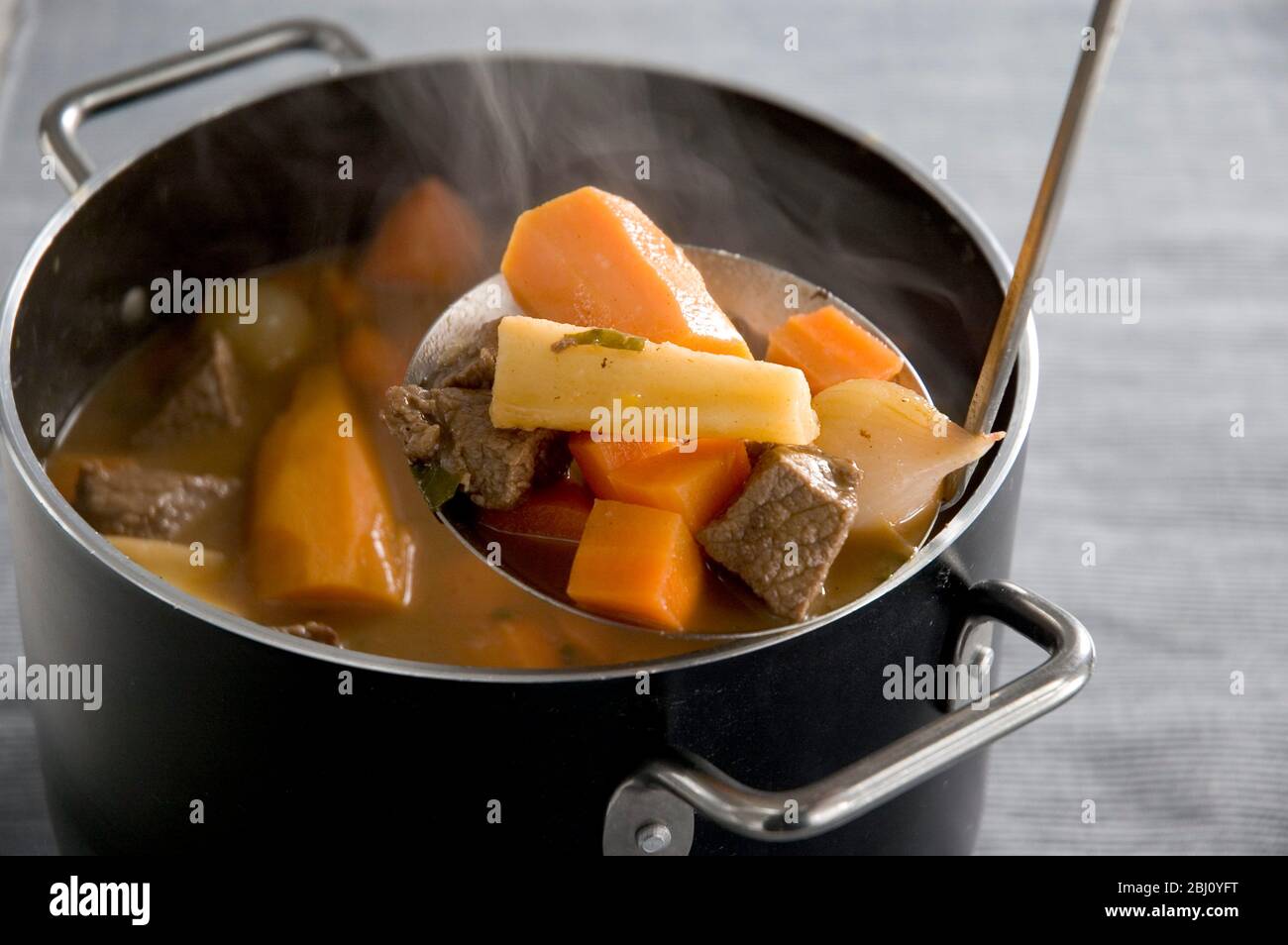 Beef stew with root vegetables with a ladle being used to serve a portion - Stock Photo