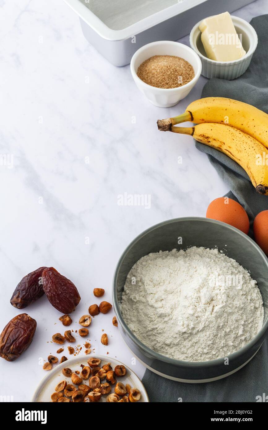 Raw ingredients on a white marble background for a hazelnut and dates banana bread recipe Stock Photo