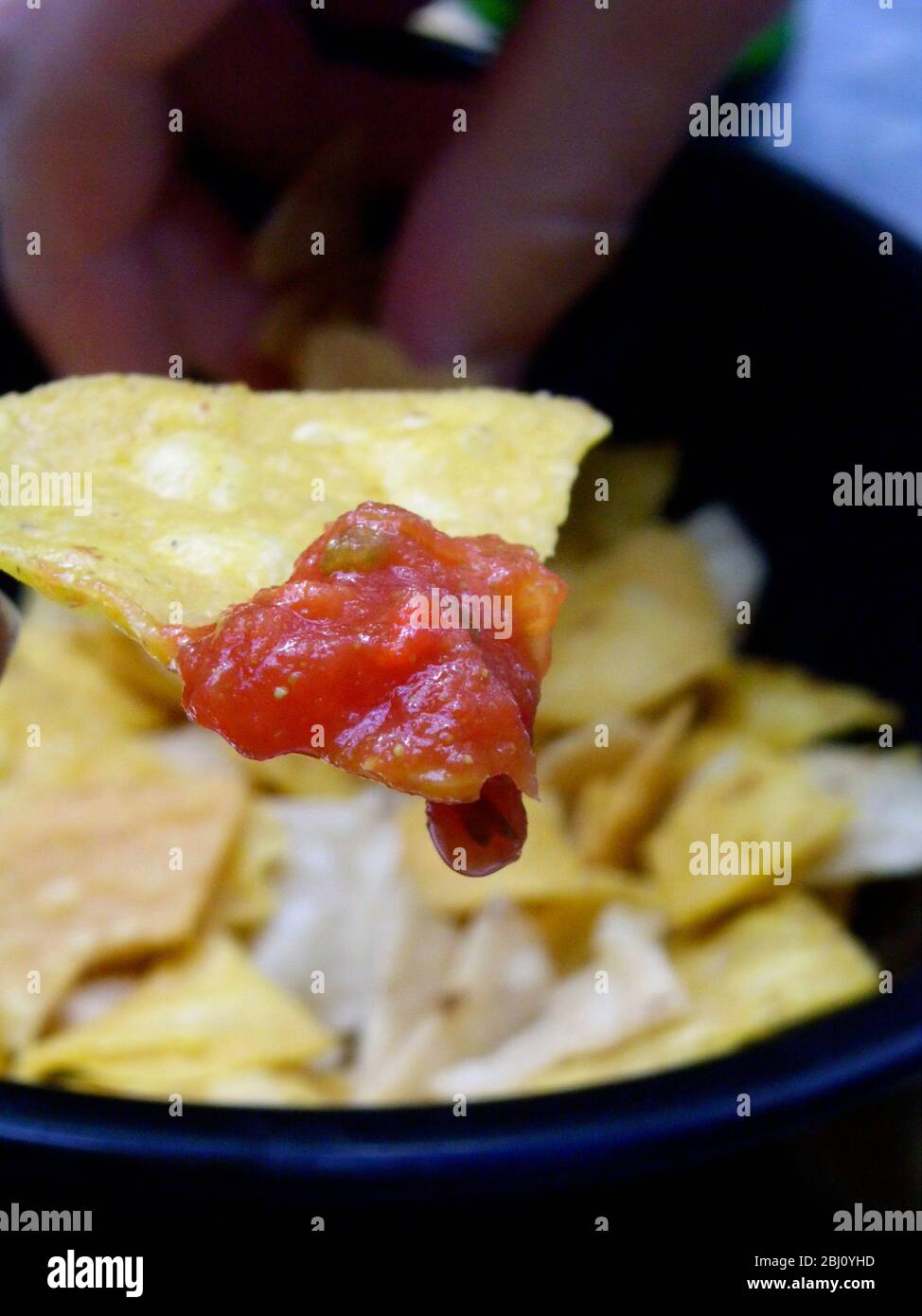 Tortilla chip dipped in salsa with more chips in background - Stock Photo
