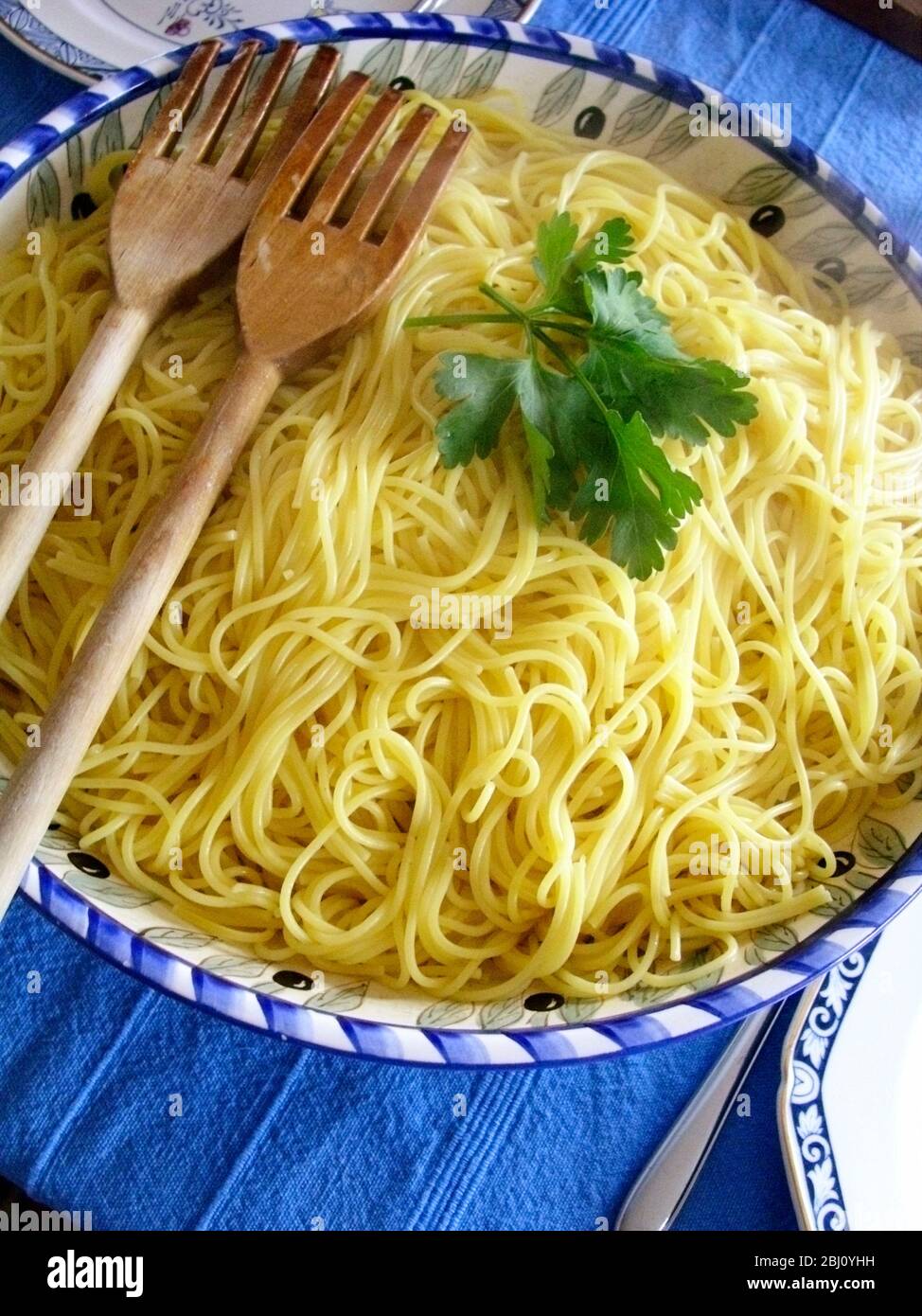 A large ceramic bowl of spaghetti garnished with flat parsley on blue cloth - Stock Photo