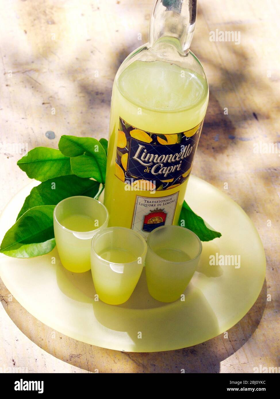 Bottle of limoncello liqueur with three glasses and lemon tree leaves - Stock Photo