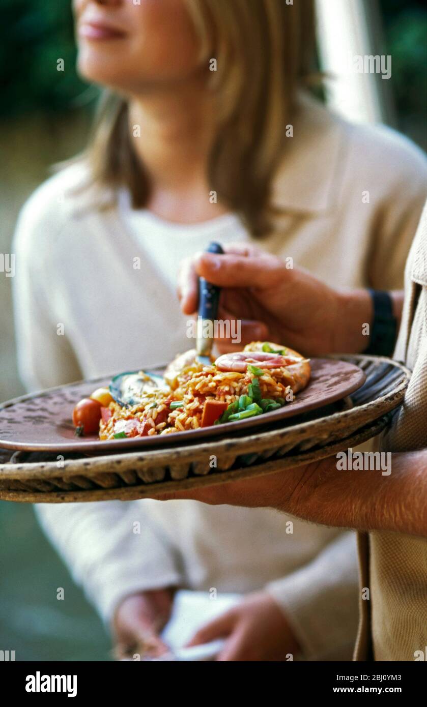 Eating rice dish on plate balanced on hand at party - Stock Photo