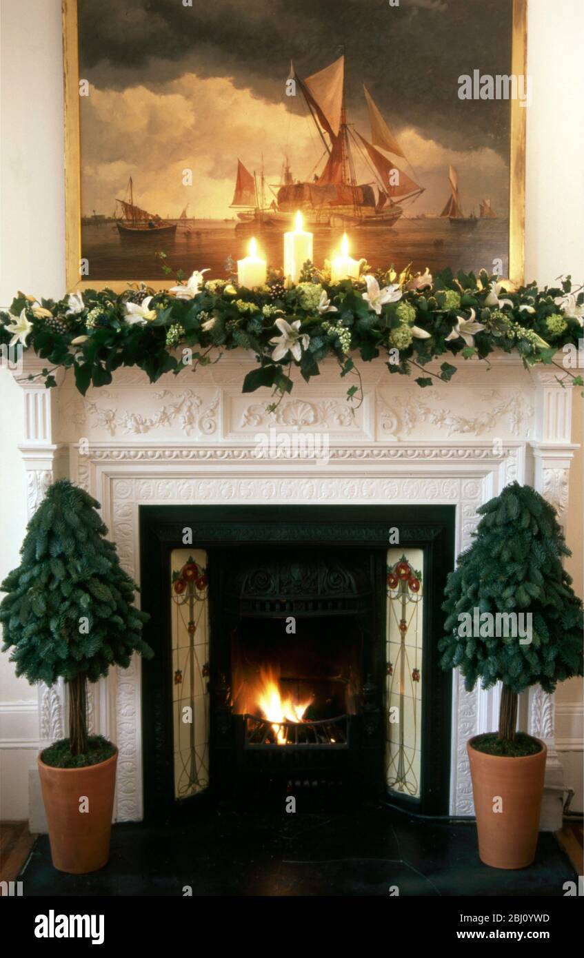 Formal fireplace with painting and burning fire, decorated for Christmas - Stock Photo