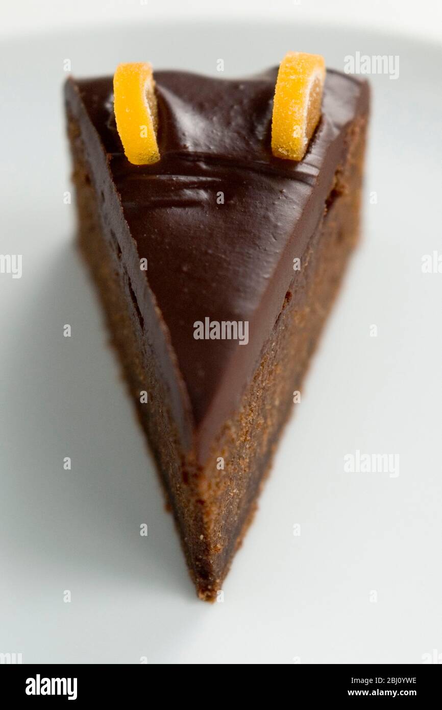 Slice of rich dense dark chocolate cake with shiny choc topping and candied orange decoration - Stock Photo