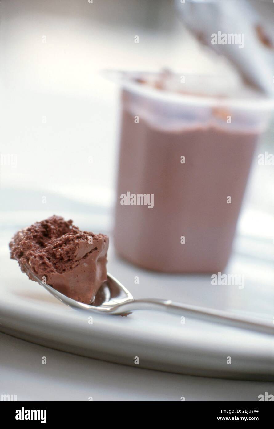 Spoonful of light chocolate shop bought mousse with open tub behind on white plate - Stock Photo