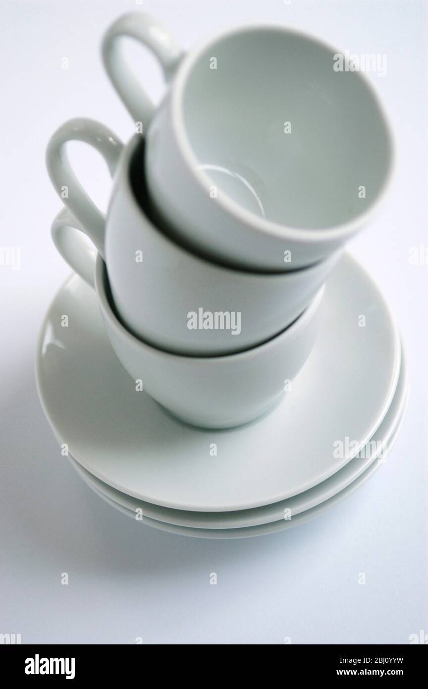 Three white coffee cups and saucers stacked up on white surface - Stock Photo