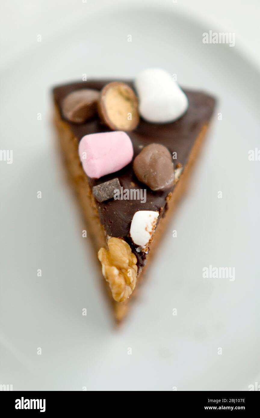 Slice of chocolate 'Rocky Road' cake topped with nuts, marshmalllows and candies - Stock Photo