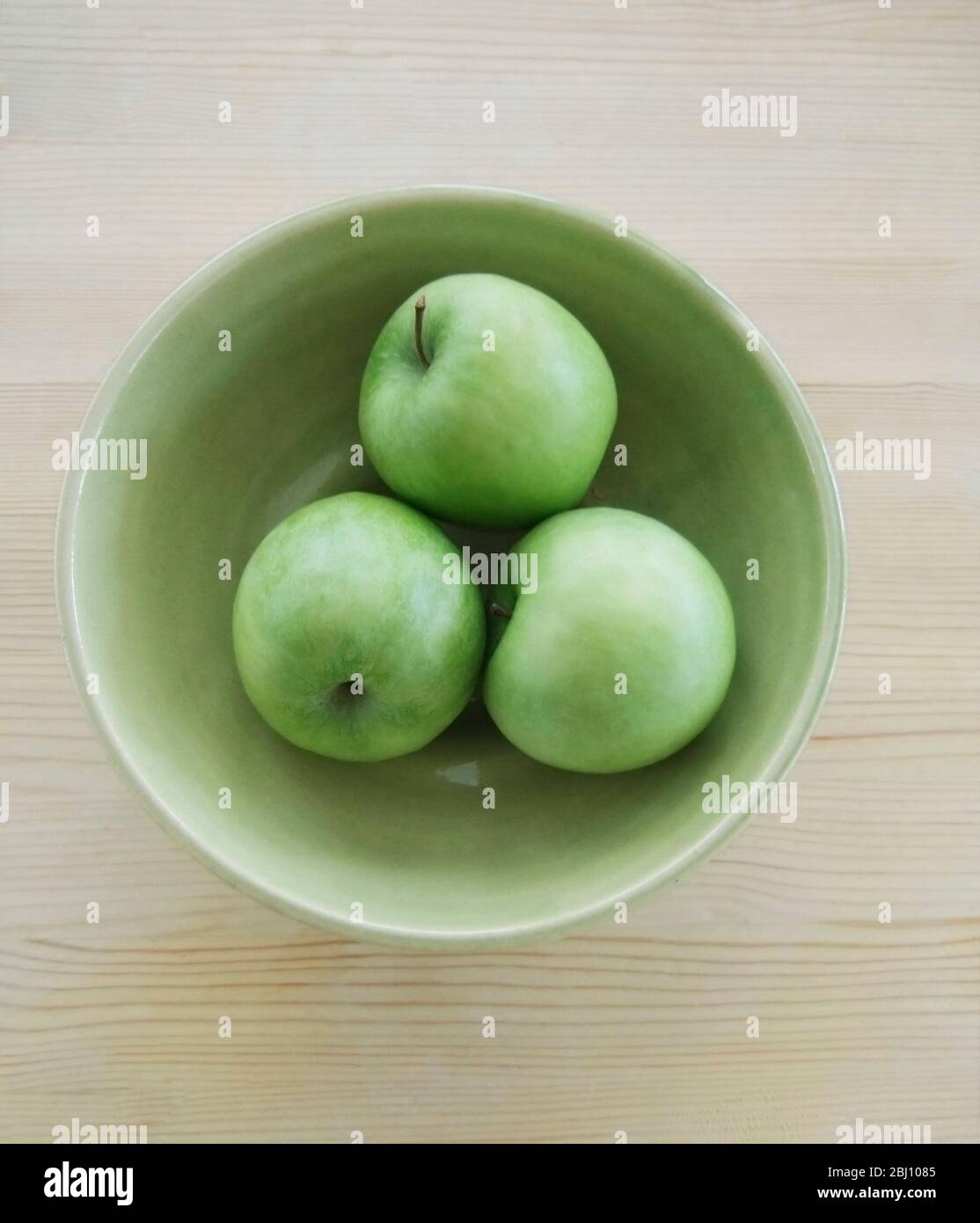 Three green Granny Smith apples in green pottery bowl Stock Photo