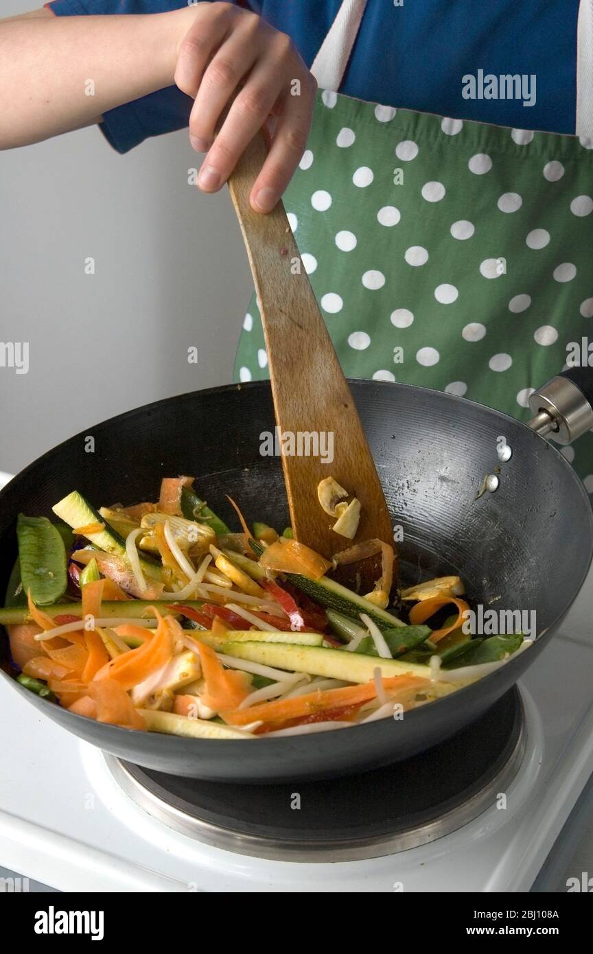 Child stirfrying shredded vegetables in wok - Stock Photo