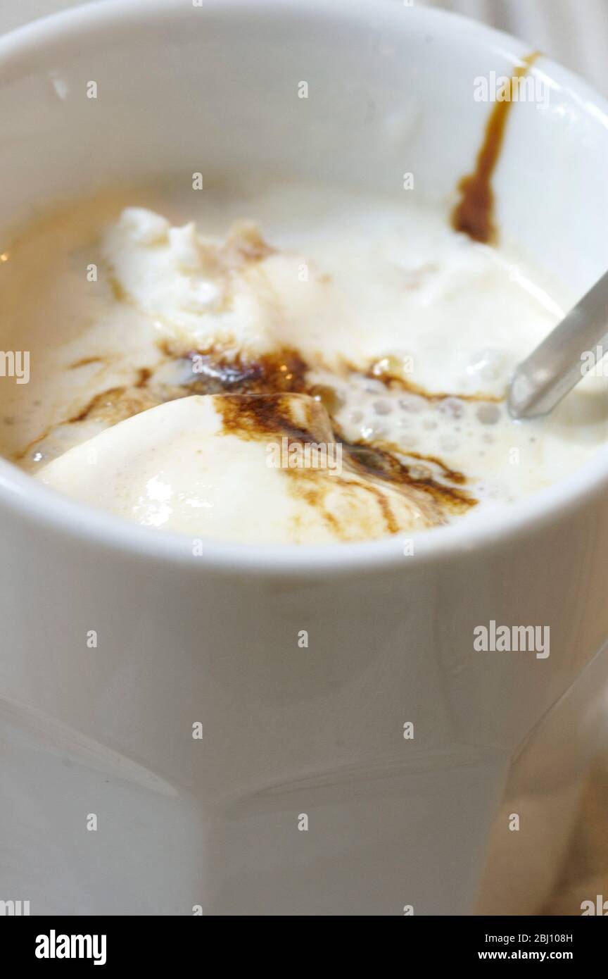 Iced coffee with vanilla icecream and chocolate syrup in white beaker on checked liinen cloth - Stock Photo