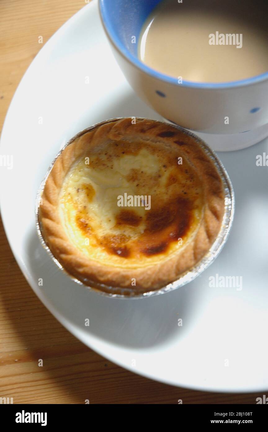 Custard tart bought from bakers with cup of tea on white plate - Stock Photo