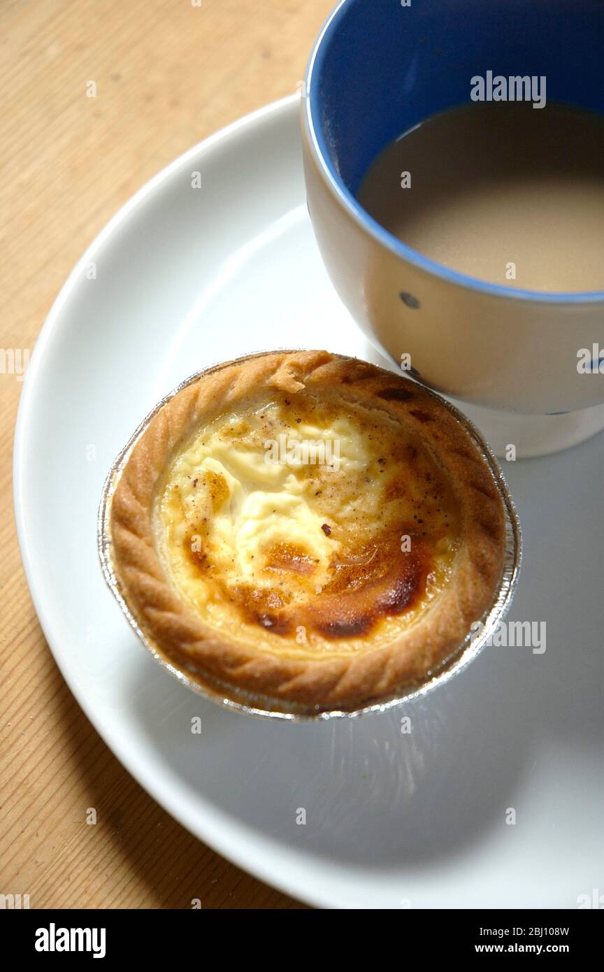 Custard tart bought from bakers with cup of tea on white plate - Stock Photo