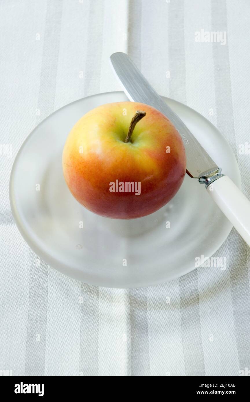 An apple on a ground glass plate with knife Stock Photo Alamy