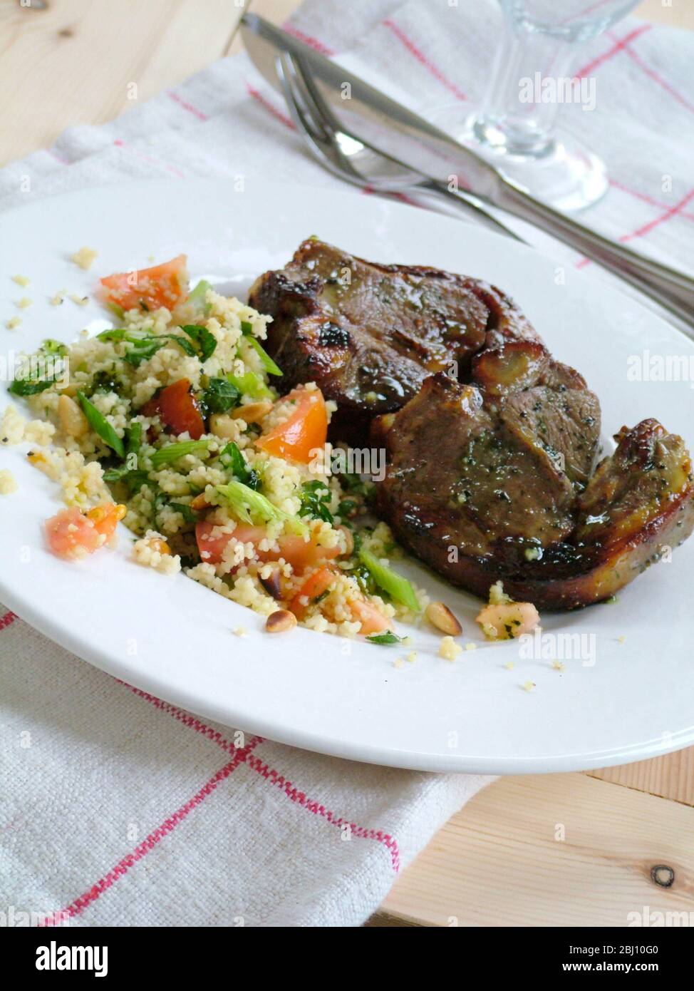 Two lamb chops with couscous with vegetables on white plate - Stock Photo