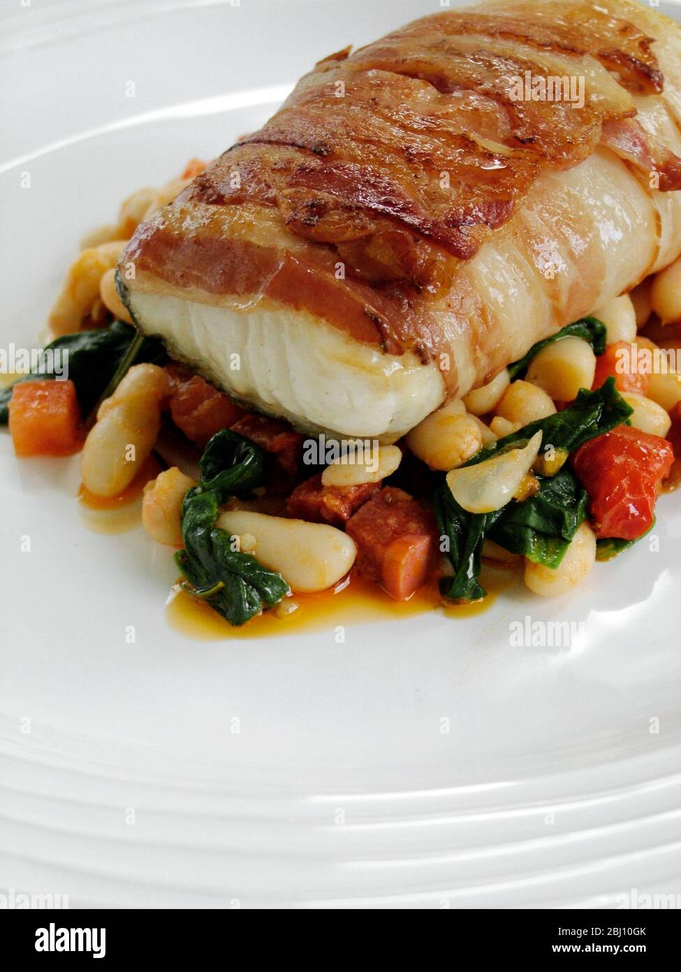 Roast monkfish loin wrapped in bacon on bed of bean casserole - Stock Photo