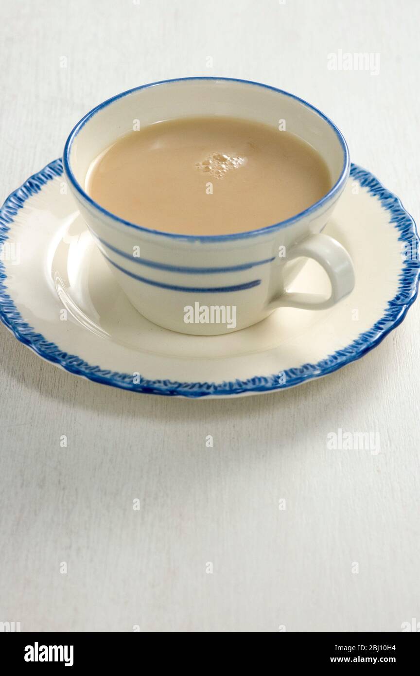 Blue and cream china cup and saucer with milky tea. - Stock Photo