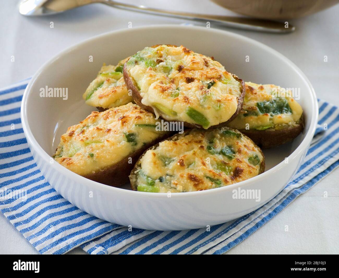 White dish of baked potato halves topped with melted cheese mixture and finished under a hot grill. Light lunch or supper dish. - Stock Photo