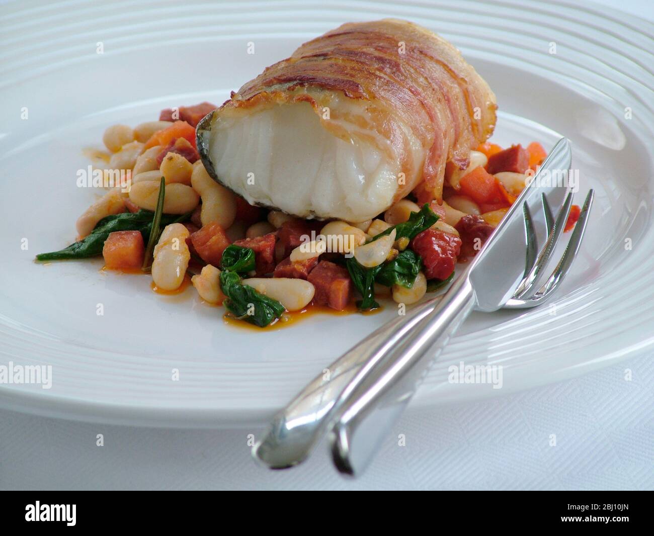 Roast monkfish loin wrapped in bacon on bed of bean casserole - Stock Photo