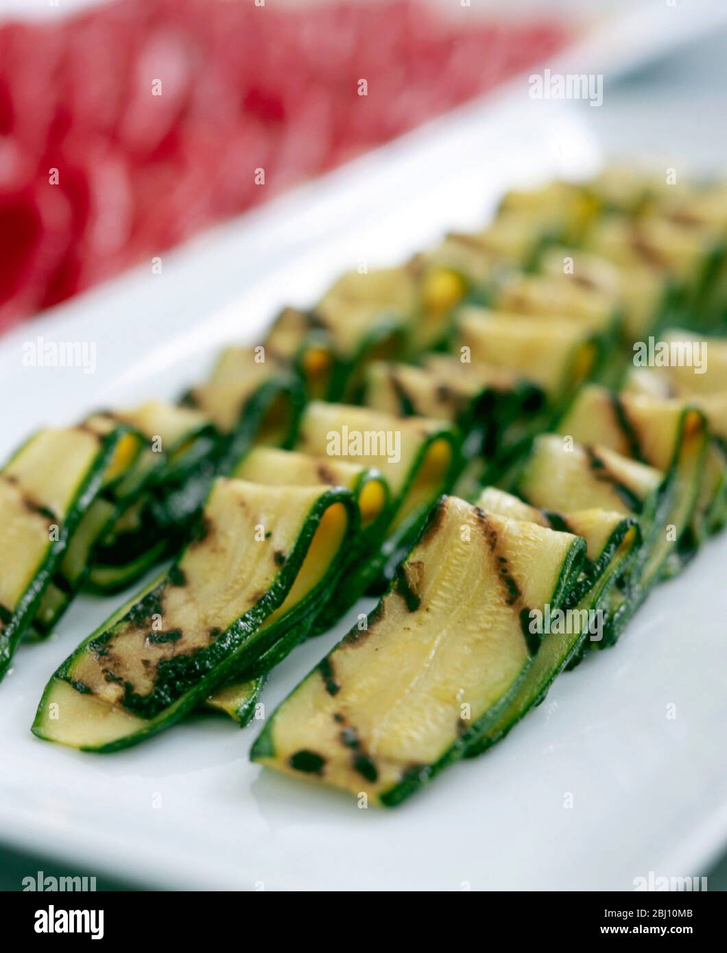 Grilled marinated courgette strips arranged on white plate - Stock Photo