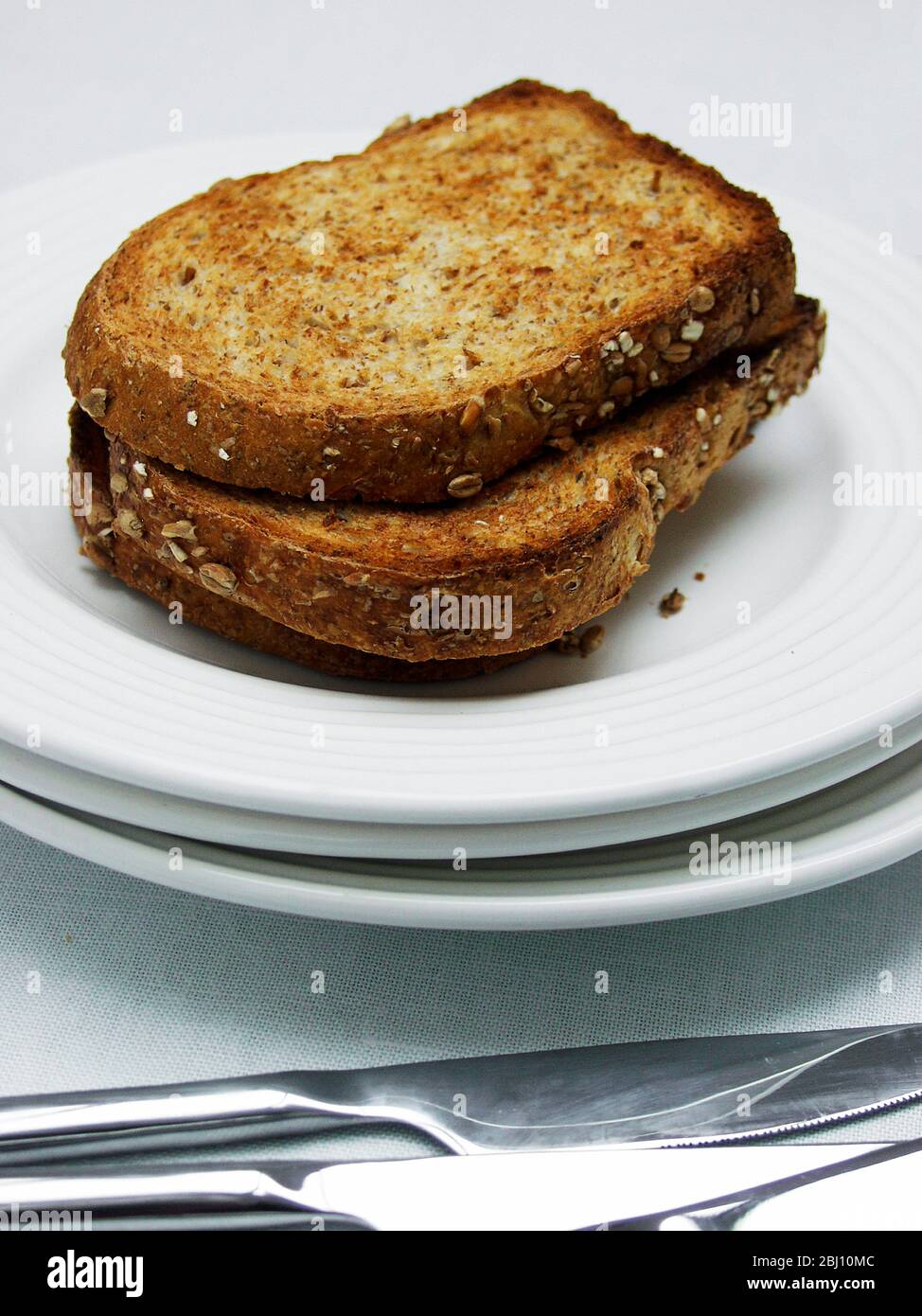 Three slices of brown wholemeal toast on a stack of white plates with