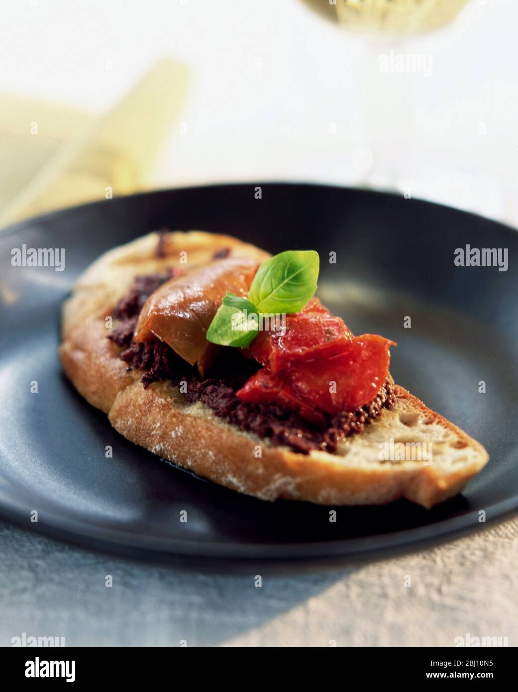 Bruschetta with olive tapenade roast tomato and parma ham topped with a basil leaf - Stock Photo