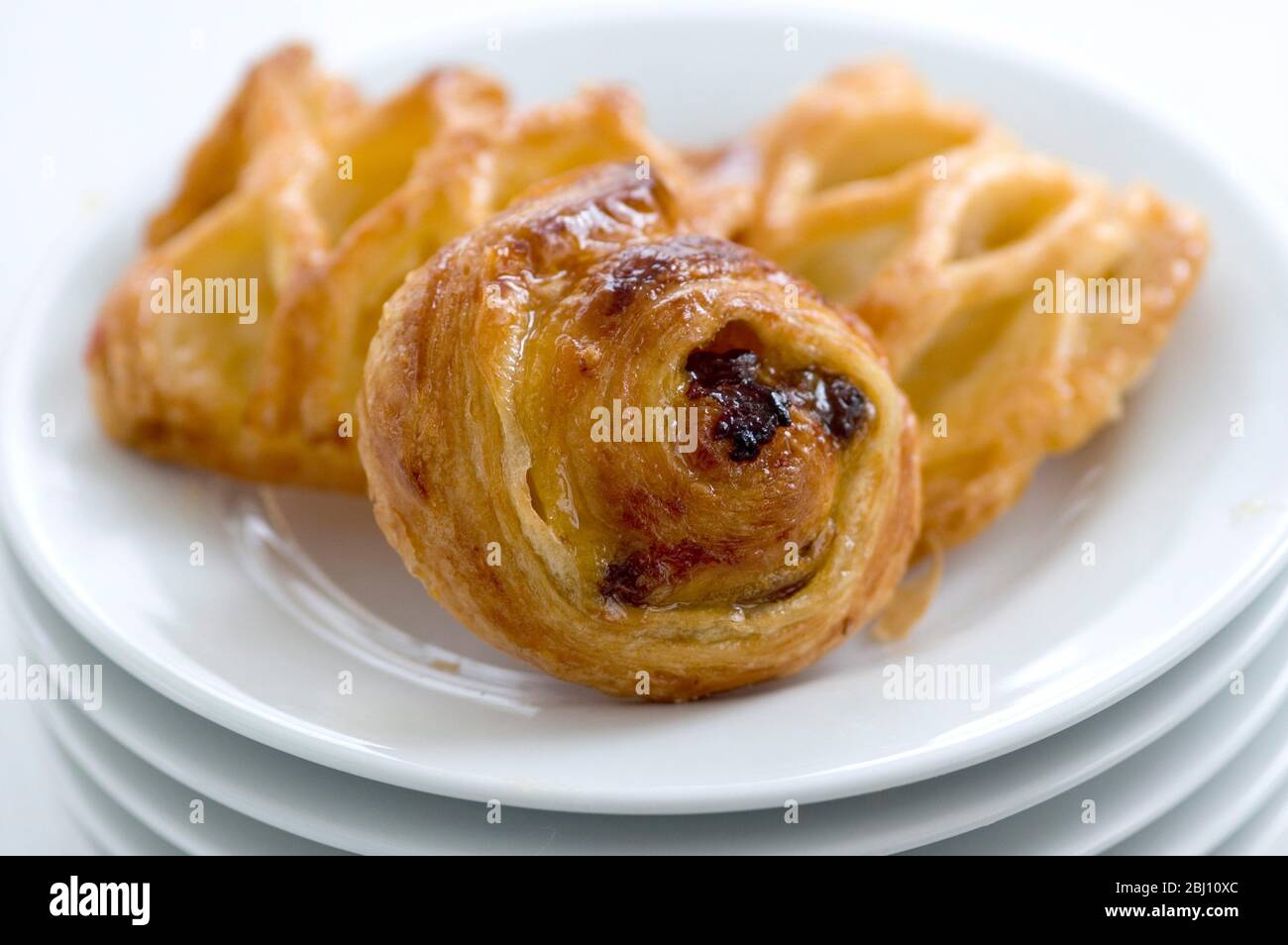 Small danish pastries on stack of white plates - Stock Photo