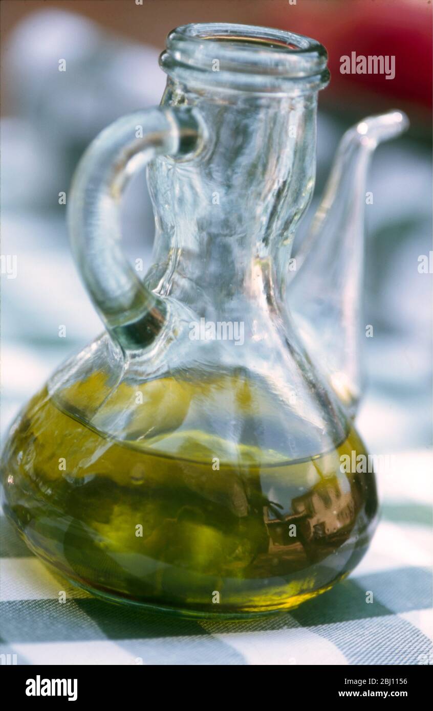 Good green olive oil in glass pourer jug on French restaurant table with village house reflected in bottle - Stock Photo