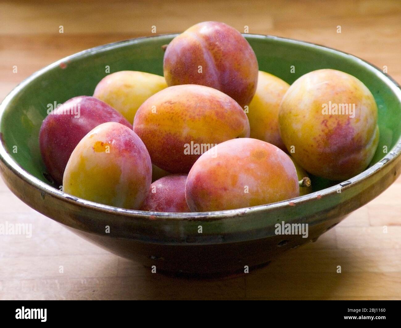 Green pottery bowl of victoria plums - Stock Photo