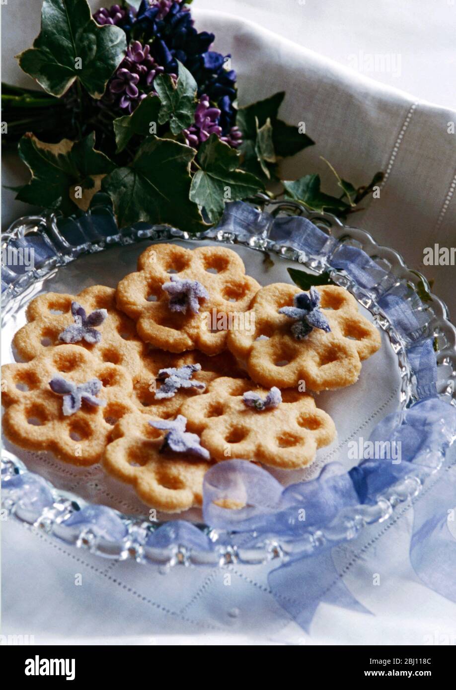 Antique glass plate threaded with mauve gauze ribbon with violet scented delicate biscuits - Stock Photo