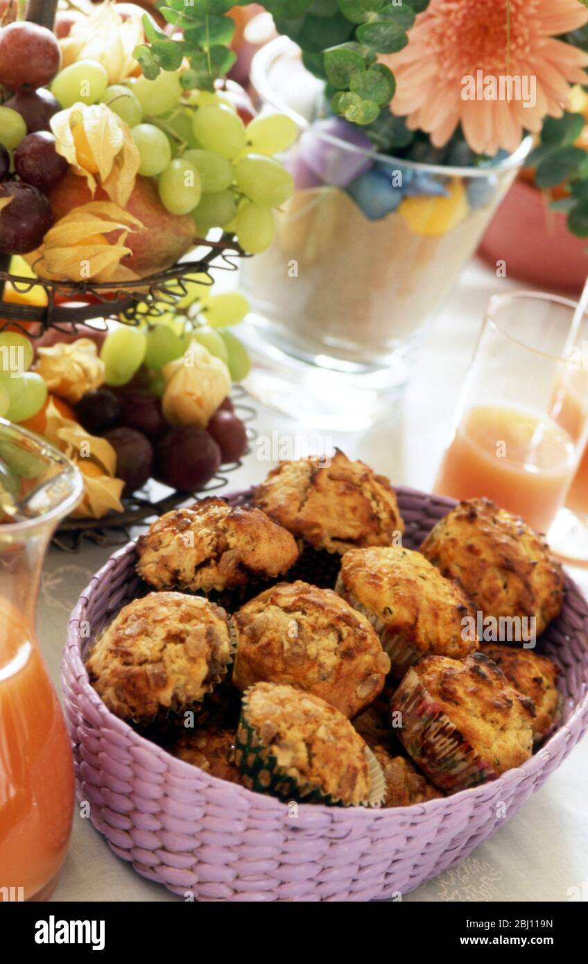 Brunch table set out with basket of bacon muffins with pink grapefruit juice and bowl of fresh fruit - Stock Photo