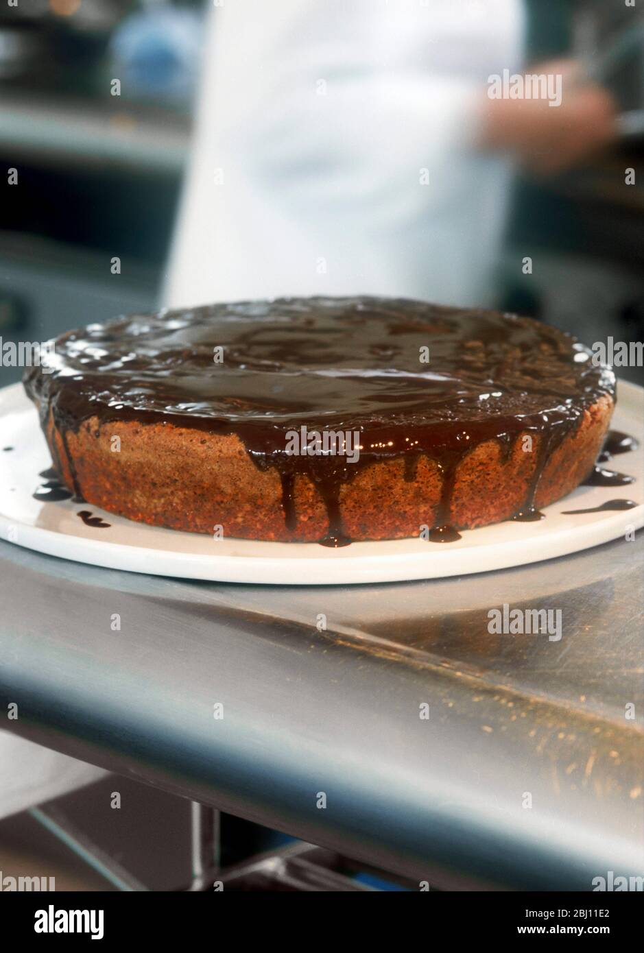 Freshly made chocolate cake with shiny topping on counter of restaurant kitchen - Stock Photo