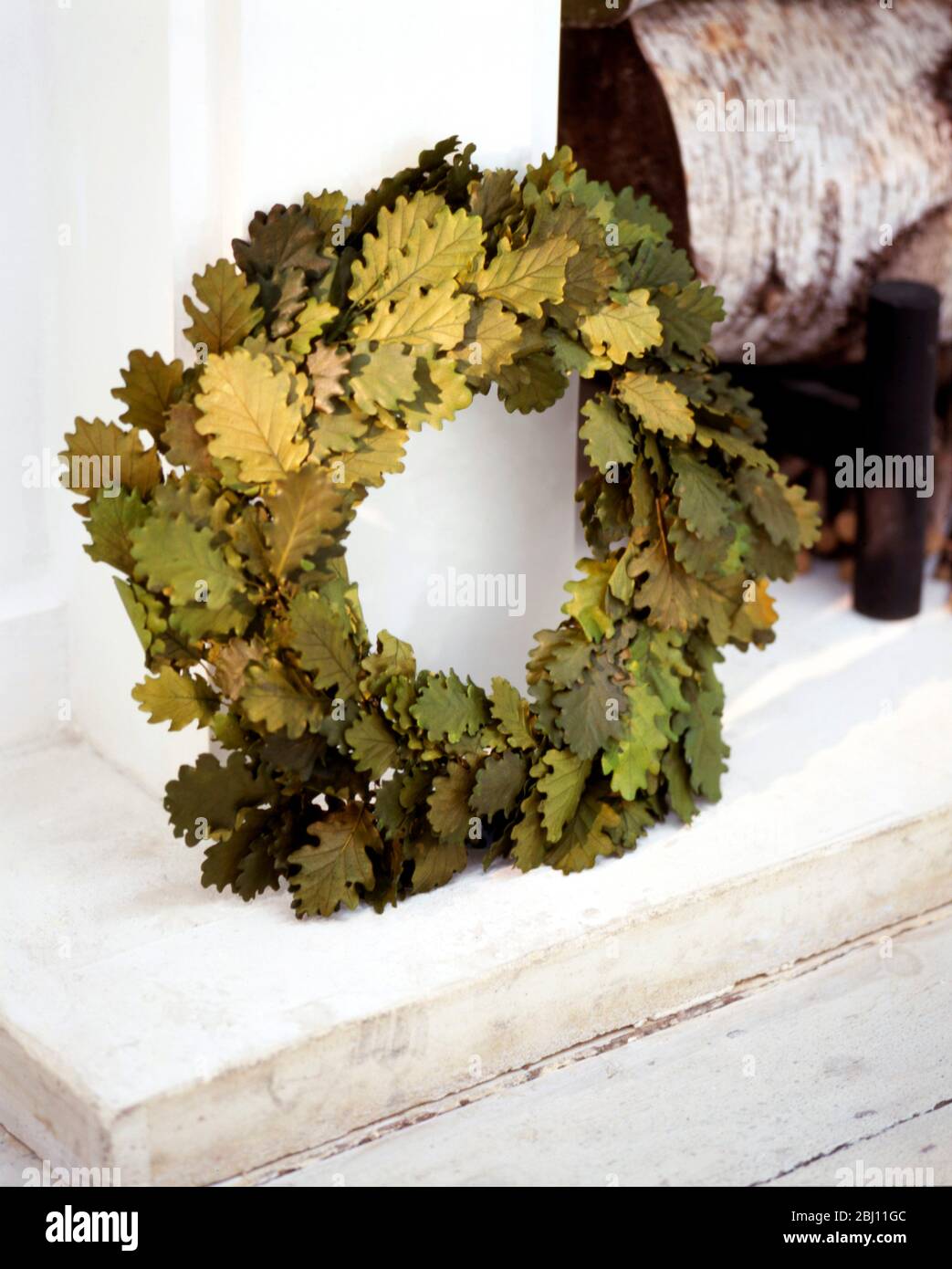 Oakleaf wreath propped as Christmas decoration on white hearth - Stock Photo