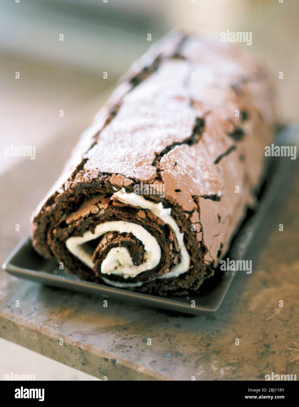 Home made chocolate roulade with cream filling, on grey plate withon marble work suface - Stock Photo