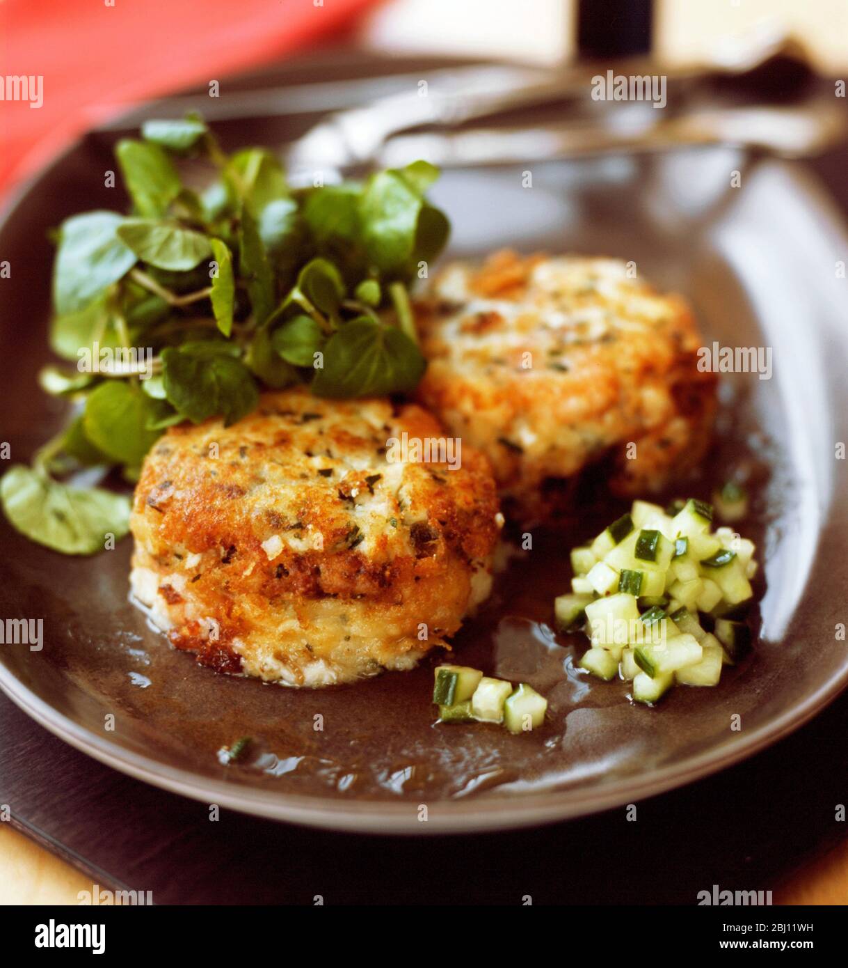 Homemade fishcakes with watercress salad and chopped cucumber in dill vinegar - Stock Photo