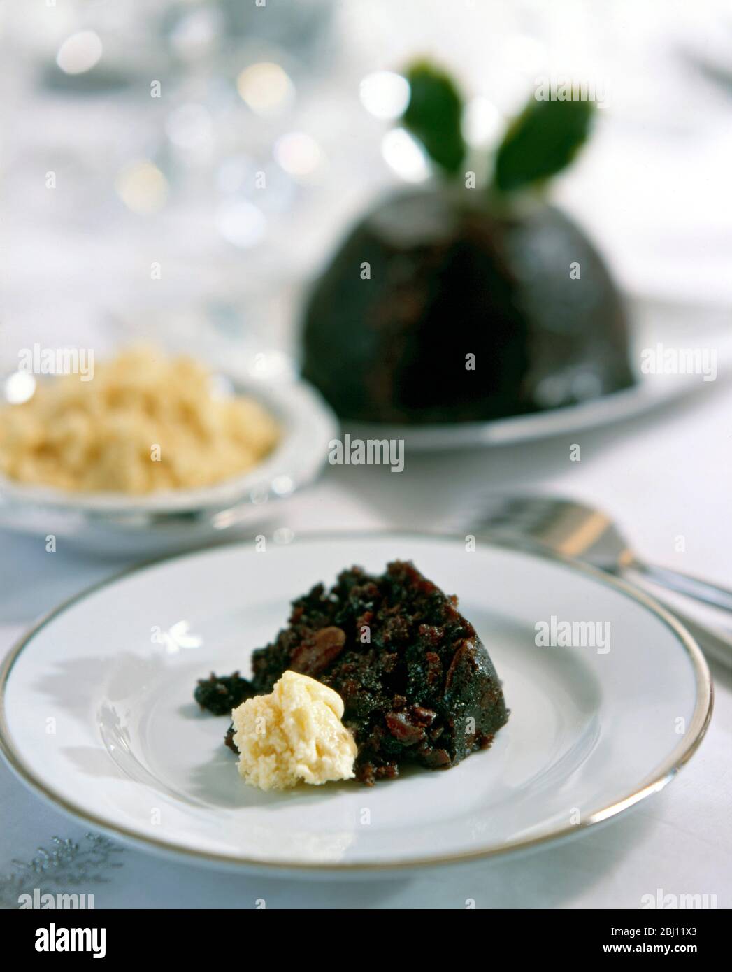 Traditional Christmas pudding on white plate in formal setting - Stock Photo