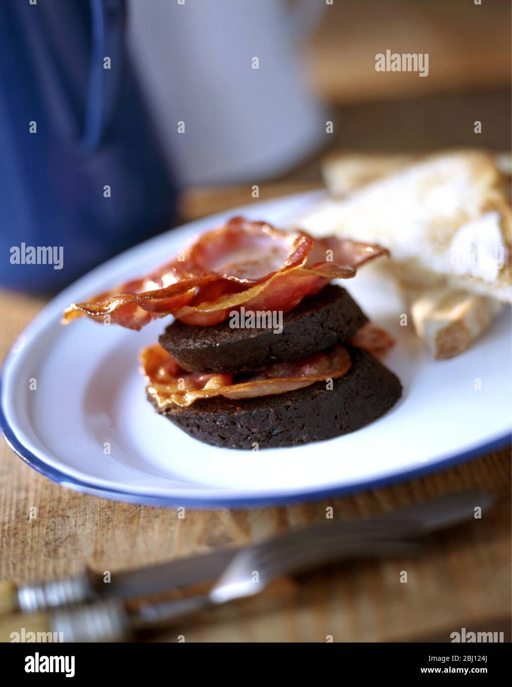 Cooked british breakfast of bacon and black pudding with white crusty bread - Stock Photo