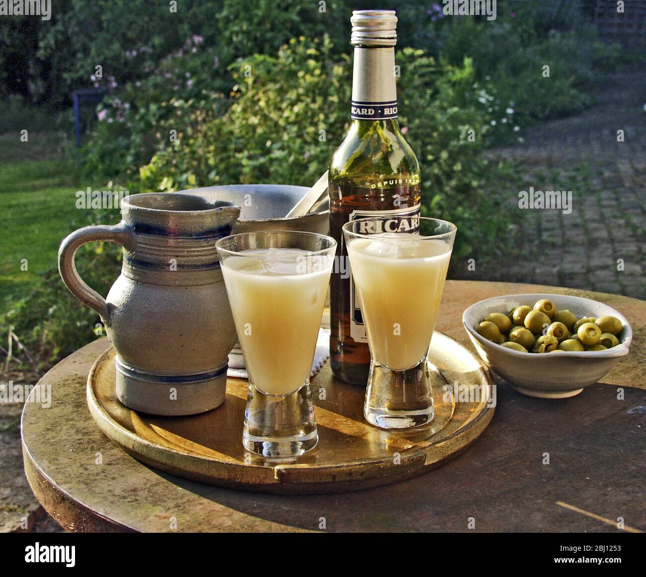 Two glasses of pernod type drink being poured in evening sunshine - Stock Photo